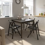 Modern dining setup with IDANÄS table & chairs, city view. Table has drawer & foldable leaf, fits elegantly in room with white decor.