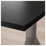 Close-up of modern, black desk edge; smooth, durable surface; supported by metal stand.