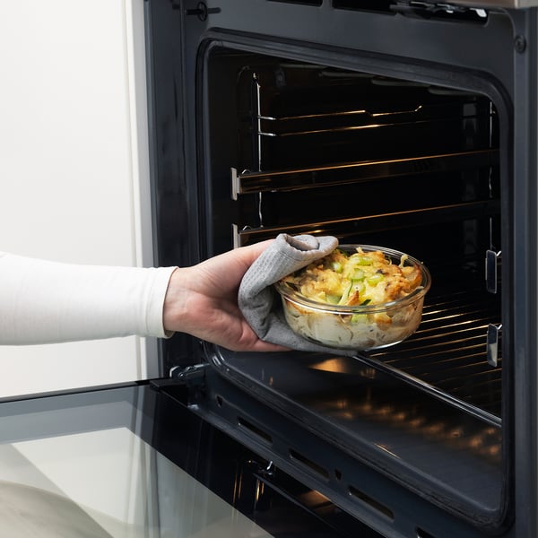 Person placing glass dish with food into oven, IKEA 365+ oven-safe container.