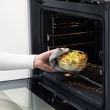 Person placing glass dish with food into oven, IKEA 365+ oven-safe container.