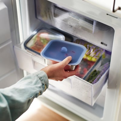 Person storing blue vacuum-sealed food container in fridge.