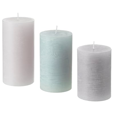 Three cylindrical candles, pastel pink, blue, and gray, stand upright in a row. Made of plant-based wax, each has a cotton wick ready to be lit.
