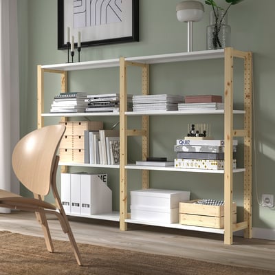 Resembles IVAR, a wooden shelf, light color, natural wood grain, rectangular shape, and holds many items. Its tall, like the chair beside it.