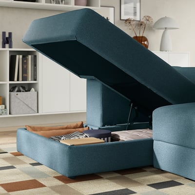 Blue modular sofa with open storage underneath, revealing cushions and blankets. Soft fabric, deep seats, and practical under-seat storage.