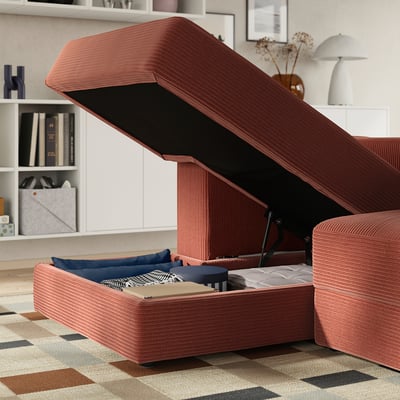 Modern red sofa with open storage underneath showing pillows, books, and linens.