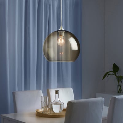 Modern dining area with a smoke-colored glass pendant light over a table set with a wooden tray, carafe, and glasses, providing ambient illumination.