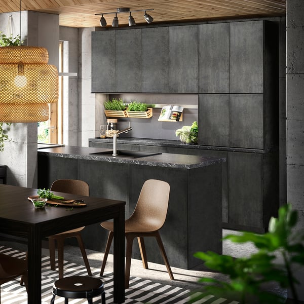 Modern kitchen with dark cabinets, wooden table, large window, pendant lamp, striped rug, and plants.