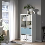 White KALLAX bookshelf with blue door, near window, holds books, decor, plants, larger than chair.