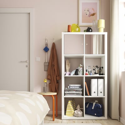 White KALLAX shelf in peach bedroom with items, colorful vase, hanging towel.