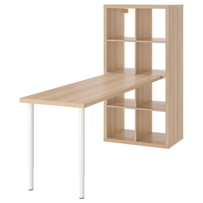 An ikea KALLAX unit with a light wooden desk attached. The unit has multiple shelves for storage and the desk is supported by white legs.