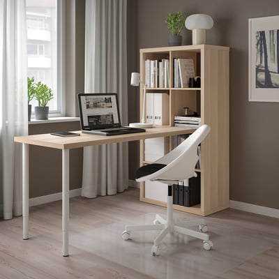 Modern home office with KALLAX beige shelving, wooden desk, laptop, white chair, and greenery.