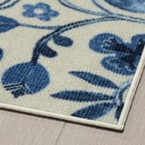 Blue and white floral area rug with intricate patterns, soft and plush texture, laid on wooden floor.