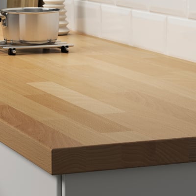 Wooden kitchen counter with smooth, natural finish. Stainless container on stove, tiled backdrop.