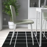 Modern dining set with green chairs, black and white checkered rug, plant, and glass.