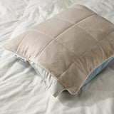 Pillow protector with cooling blue and warming beige sides on a bed, showcasing its dual comfort feature.