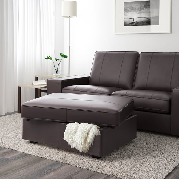 Dark leather living room set with ottoman, featuring storage underneath. White throw blanket resting on ottoman.