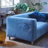 Unique blue denim sofa with metal legs, jeans pocket, eco-friendly & recycled, by a window with plants.