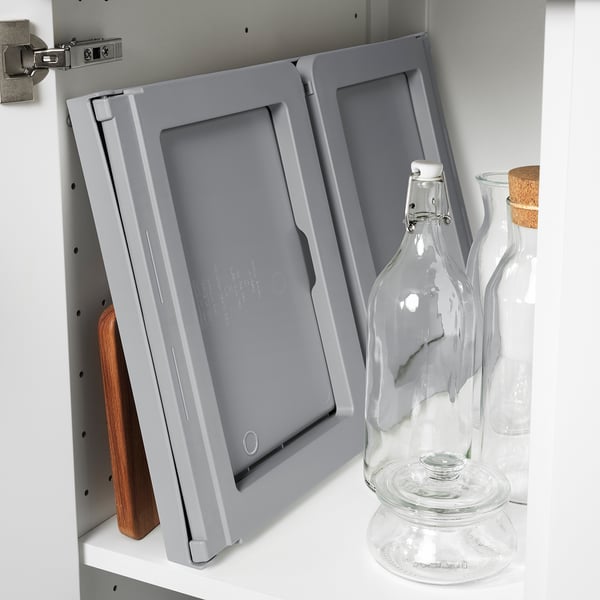 Gray KLIPSK bed tray stored vertically, leaning against cabinet, with glass jars beside it.
