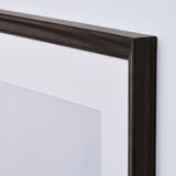 Dark wood picture frame with clear plastic covering, leaning against white wall.