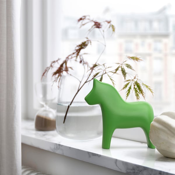 Bright green ceramic dala horse figure, smaller than vase, on marble shelf.