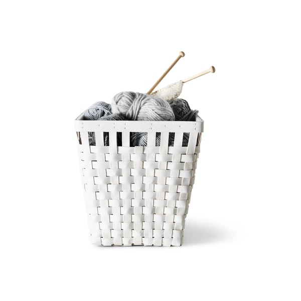Knitted grey yarn and wooden needles in woven white basket.