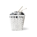 Knitted grey yarn and wooden needles in woven white basket.