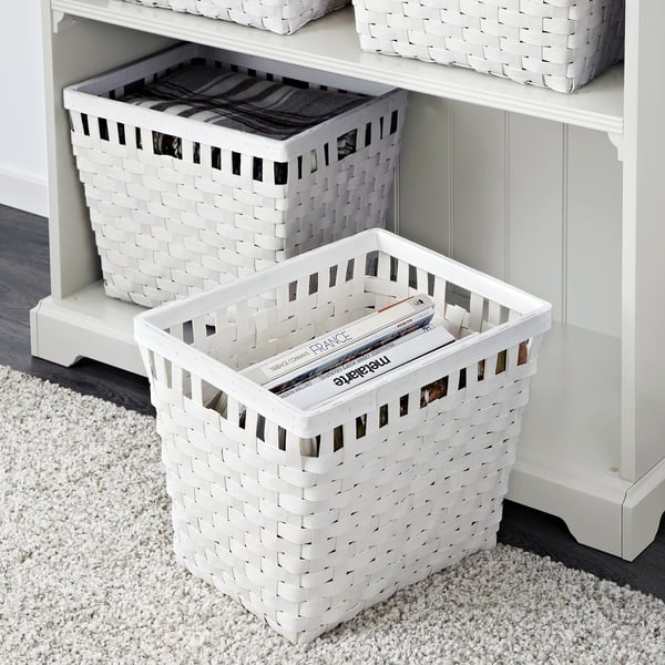 White woven baskets stored on shelves. Bottom basket holds magazines; top holds folded fabric.