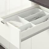 Open kitchen drawer with cutlery organizer: spoons, forks, knives in separate sections.