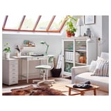 Cozy home office with white desk, green chair, and natural light from skylights, featuring plants and organized decor.