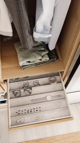 Wooden wardrobe drawer with felt-lined jewelry tray, folded clothes, blue stripes and grey sweaters.