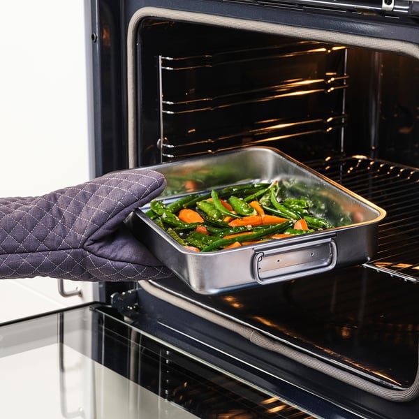 Person in oven mitts placing metal tray with colorful vegetables into oven.