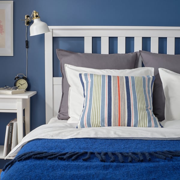 Cozy bed with blue walls, white headboard, striped pillow, grey pillows, and blue blanket.
