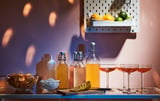 KORKEN glass jars with silicon stopper, holding drinks, ice, snacks, and lemons, placed on blue shelf under fruits basket.