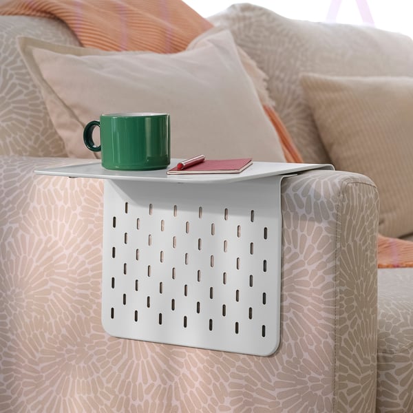 A green mug on a white armrest tray hanging from a sofa, holding a notebook and pen.