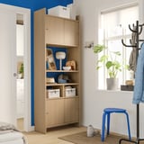 Modern entryway with light wood LÅDMAKARE cabinet, blue accents, plant, and coat rack.