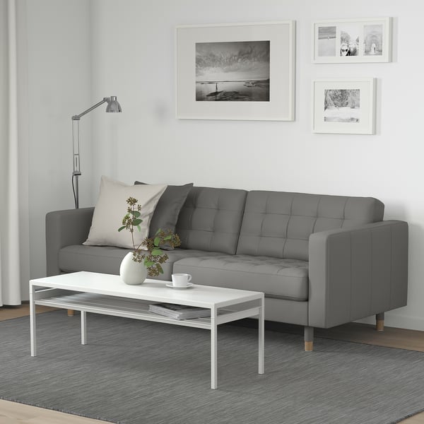 Modern living room with grey sofa, white table, rug, lamp, and black-and-white wall art.