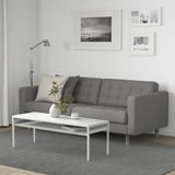 Modern living room with grey sofa, white table, rug, lamp, and black-and-white wall art.