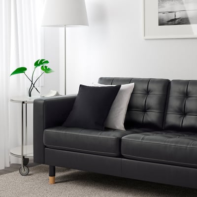 Modern living room with black leather sofa, two pillows, and a side table with a plant.