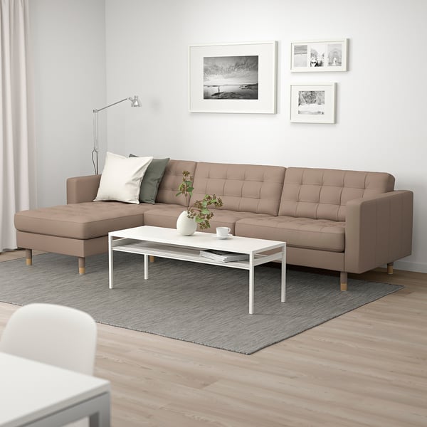 Modern living room with l-sofa, colorful cushions, rug, coffee table, art, lamp, and plant.