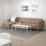 Modern living room with l-sofa, colorful cushions, rug, coffee table, art, lamp, and plant.