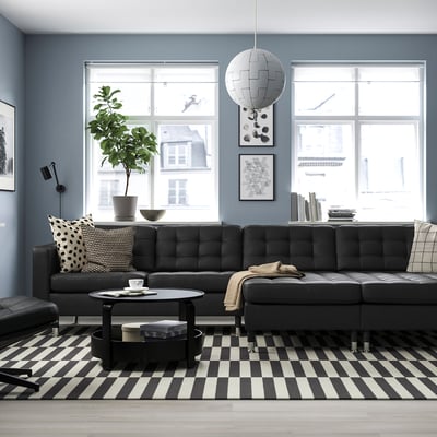 Modern black LANDSKRONA sofa with plush cushions and tufted leather, paired with a checked rug, large windows, and round coffee table.