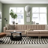 Modern living room: large beige sofa, black coffee table, striped rug, green walls, large windows, hanging globe light.