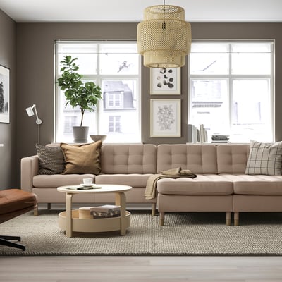 Modern living room with large tan sectional sofa, wooden coffee table, large window, plant, hanging lamp, and art on wall.