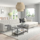 Modern living room with large, l-shaped cream-colored LANDSKRONA sofa, glass coffee table, wicker pendant light, and large windows with curtains.