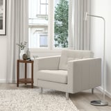A beige LANDSKRONA armchair near a large window, with a floor lamp and decorative table beside it.