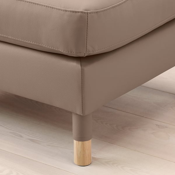 Close-up of a high-quality leather footstool with wood legs on a hardwood floor.