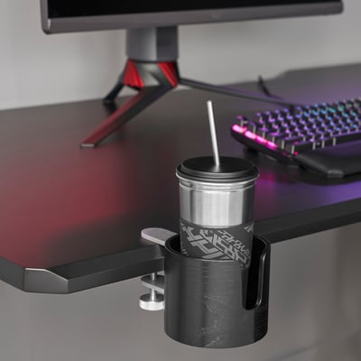 Black desk with monitor, keyboard, and a mug in a holder. The mug has a lid and straw, and a silicone sleeve for grip.
