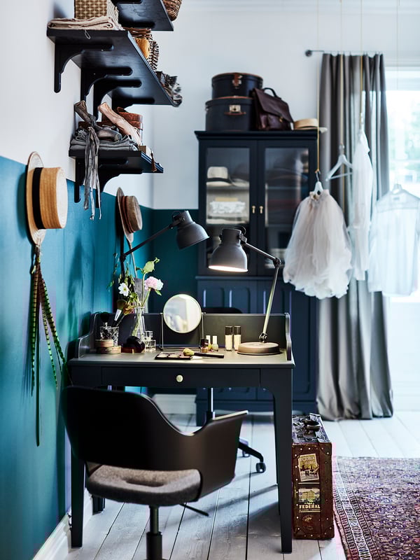 Stylish home office: black desk, blue wall, mirror, lamp, art, grey curtains, rug, chair.