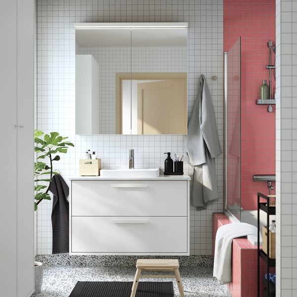 Modern bathroom white LETTAN mirror cabinet above sink, grey towels, red-tiled shower, and black plant.