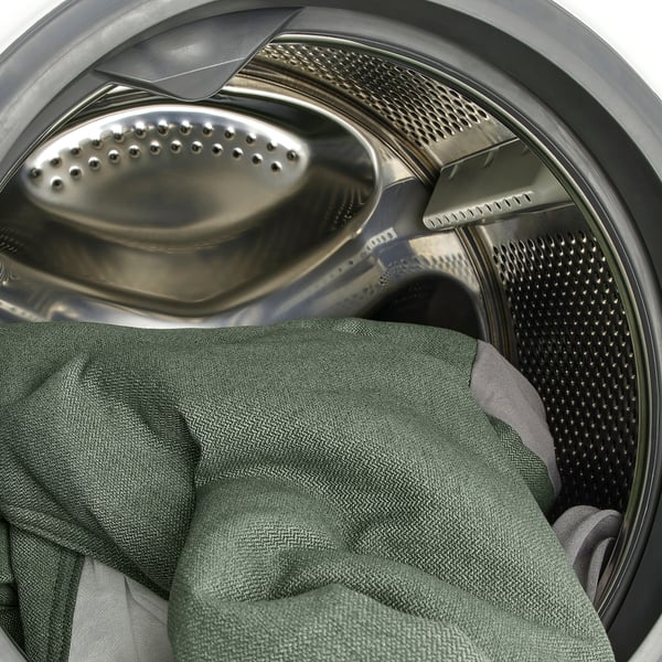 Washing machine drum with green towel, perforated metal interior, and rubber seal visible.